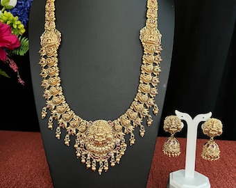 May include: A gold necklace with a pendant featuring a deity, adorned with green and red stones. Matching earrings with similar design and stones.