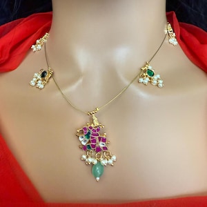 May include: A gold necklace with a pink and green pendant featuring a floral design. The pendant is adorned with white pearls and green stones. The necklace also has two smaller pendants with green stones and white pearls.