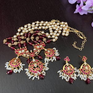 May include: A gold necklace with a multi-strand pearl and burgundy bead design. The necklace has three pendant charms with burgundy stones and white pearls. Matching earrings with burgundy stones and white pearls.