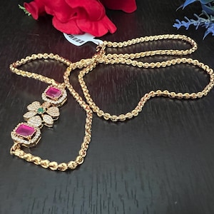 May include: A gold chain necklace with a pendant featuring three pink and green gemstones surrounded by clear stones. The chain is a rope style.
