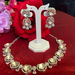 May include: A silver necklace and earrings set with clear stones. The necklace has a geometric design with multiple large stones and smaller stones around the edges. The earrings are drop earrings with two large stones.