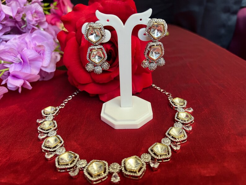 May include: A silver necklace and earrings set with clear stones. The necklace has a geometric design with multiple large stones and smaller stones around the edges. The earrings are drop earrings with two large stones.