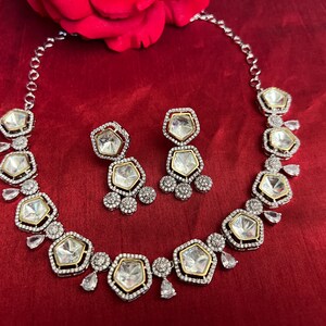 May include: A silver and gold necklace and earrings set with clear, faceted stones. The necklace has a row of octagonal stones with smaller stones around them. The earrings have two octagonal stones with smaller stones around them.