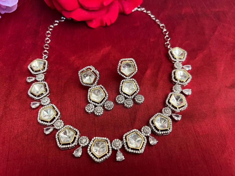 May include: A silver and gold necklace and earrings set with clear, faceted stones. The necklace has a row of octagonal stones with smaller stones around them. The earrings have two octagonal stones with smaller stones around them.