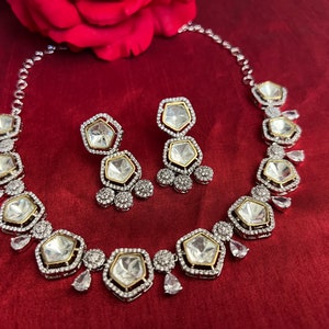 May include: A silver and gold necklace and earrings set with large, clear, faceted stones set in a geometric shape. The stones are surrounded by smaller, clear stones.