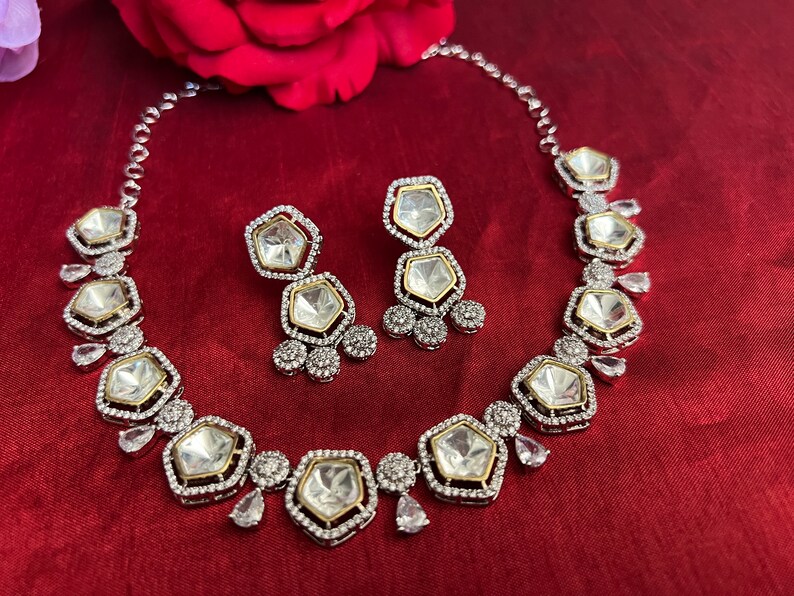 May include: A silver and gold necklace and earrings set with large, clear, faceted stones set in a geometric shape. The stones are surrounded by smaller, clear stones.