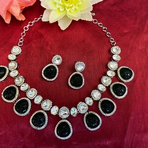 Pu&ograve; includere: Un set di collana e orecchini nero e argento con pietre nere intagliate e strass trasparenti. La collana ha una catena d'argento e gli orecchini sono a goccia.
