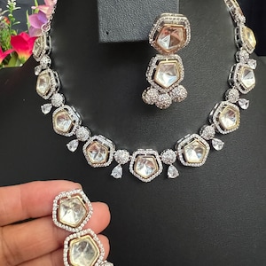 May include: A silver and gold necklace and earrings set with clear stones. The necklace has a geometric design with multiple layers of stones. The earrings are drop earrings with a similar design.
