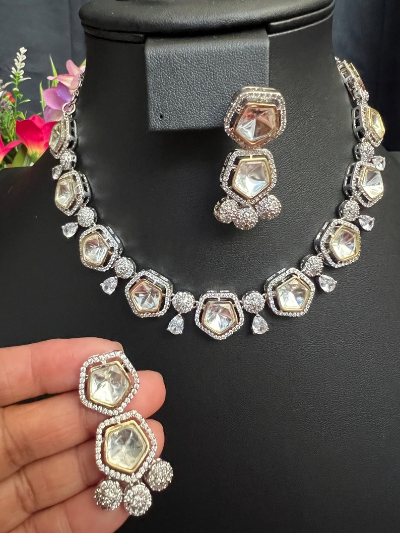 May include: A silver and gold necklace and earrings set with clear stones. The necklace has a geometric design with multiple layers of stones. The earrings are drop earrings with a similar design.