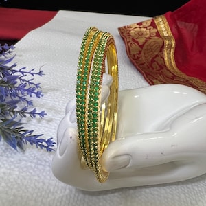 May include: Set of four gold bangles with green emerald-like stones set in a row around each bangle.
