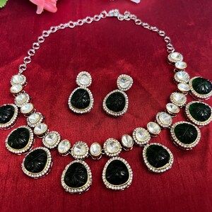 Pu&ograve; includere: Una collana d'argento con un designo bianco e nero. La collana ha un ciondolo con una pietra verde intagliata. La collana &egrave; accompagnata da orecchini abbinati.