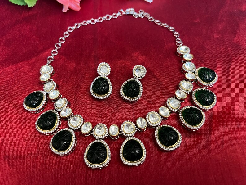 Pu&ograve; includere: Una collana d'argento con un designo bianco e nero. La collana ha un ciondolo con una pietra verde intagliata. La collana &egrave; accompagnata da orecchini abbinati.