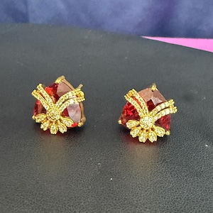 May include: A pair of gold earrings with red gemstone accents and clear crystal embellishments.