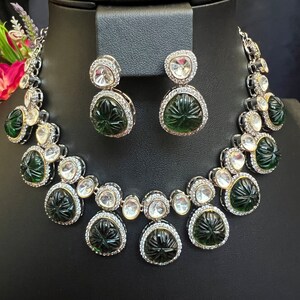 Pu&ograve; includere: Un set di collana e orecchini verde e argento con pietre verdi intagliate e strass trasparenti.