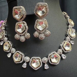 May include: A silver and gold necklace and earrings set with large clear faceted stones. The necklace has a row of stones with smaller stones around them. The earrings have a single large stone with smaller stones around it.