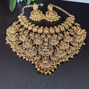 May include: A gold-tone necklace and earrings set with intricate floral and geometric designs. The necklace features a large pendant with a central figure and is adorned with small, round beads.
