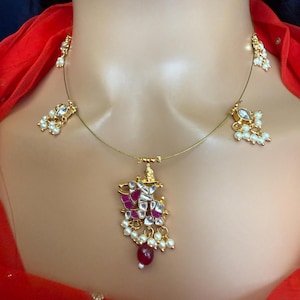 May include: A gold necklace with a pink and white pendant and pearl accents. The pendant features a geometric design with a red stone at the bottom.