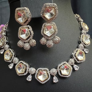 May include: A silver and gold necklace and earrings set with large clear faceted stones. The necklace has a row of stones with smaller stones around them. The earrings have a single large stone with smaller stones around it.