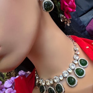 Pu&ograve; includere: Una collana d'argento con un ciondolo di pietra verde e accenti di cristallo trasparente. La collana &egrave; su un manichino che indossa una blusa rossa.