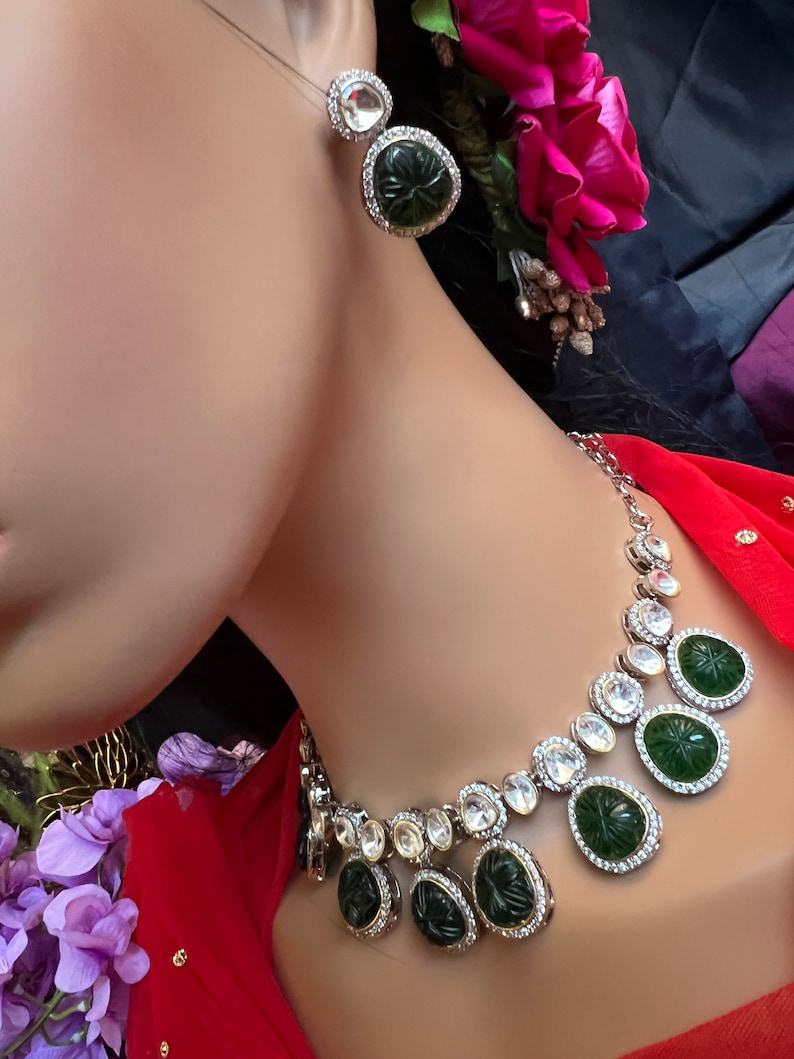 Pu&ograve; includere: Una collana d'argento con un ciondolo di pietra verde e accenti di cristallo trasparente. La collana &egrave; su un manichino che indossa una blusa rossa.