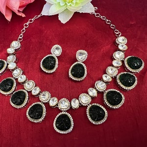 Pu&ograve; includere: Una collana d'argento con un set di ciondoli bianco e nero. La collana ha una catena d'argento ed &egrave; adornata con piccole pietre bianche. Il ciondolo &egrave; una pietra nera intagliata con un motivo floreale. Il set include anche un paio di orecchini abbinati.