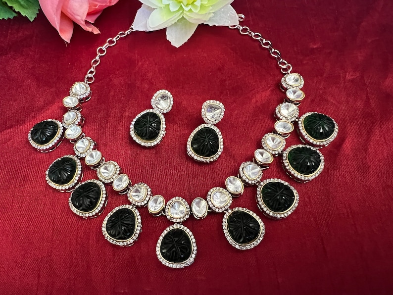Pu&ograve; includere: Una collana d'argento con un set di ciondoli bianco e nero. La collana ha una catena d'argento ed &egrave; adornata con piccole pietre bianche. Il ciondolo &egrave; una pietra nera intagliata con un motivo floreale. Il set include anche un paio di orecchini abbinati.