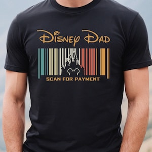 May include: Black t-shirt with a vintage-style graphic that says "Disney Dad" with a barcode and a silhouette of Cinderella's castle and Mickey Mouse. The text below the barcode says "Scan for Payment".