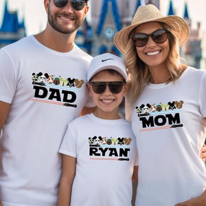 May include: Three people wearing white t-shirts with Disney character designs and text. The shirts say "DAD", "RYAN", and "MOM" with a lightsaber graphic. The background features a castle.