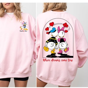 May include: Pink sweatshirt with a cartoon image of Donald and Daisy Duck on the back. The text "Where dreams come true" is printed below the image. The front of the sweatshirt has a smaller image of Donald and Daisy Duck with the text "Say it with a Duck".