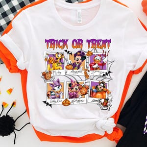 May include: White t-shirt with a Halloween-themed graphic featuring Disney characters. The design includes the text "Trick or Treat" in purple, along with images of Pluto, Mickey Mouse, Donald Duck, Daisy Duck, Minnie Mouse, and Goofy in Halloween costumes.
