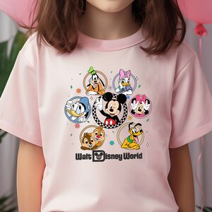 May include: Pink short-sleeved t-shirt with a colorful graphic of Mickey Mouse and other Disney characters in a circle. The text "Walt Disney World" is printed below the graphic.