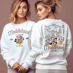 May include: White sweatshirt with a colorful graphic of Mickey Mouse and friends in front of Cinderella's Castle. The text "Maddieland Est. 2023 Texas" is printed on the front of the sweatshirt.