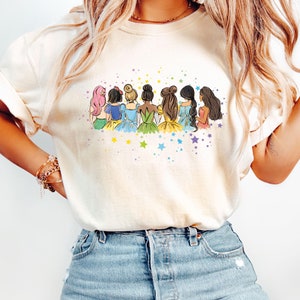 May include: A white t-shirt with a graphic of seven cartoon princesses standing back to back with a rainbow of colors and stars.