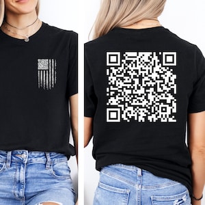 May include: A black t-shirt with a white distressed American flag design on the front and a white QR code on the back. The model is wearing blue jeans with distressed details.