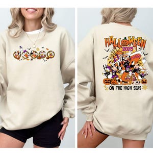 May include: A beige sweatshirt with a Halloween-themed graphic. The front features cartoon characters in circular frames, and the back displays "Halloween 2025" with pumpkins and characters, and the text "On The High Seas".