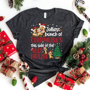 May include: A dark gray t-shirt with a Christmas-themed design featuring two cartoon chipmunks wearing Santa hats and the text "Jolliest bunch of Chipmunks this side of the Nut House".