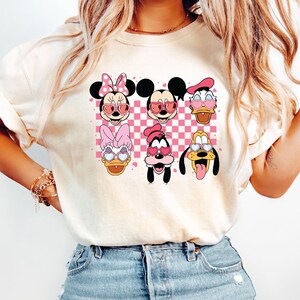 May include: A white t-shirt with a checkered pattern and images of Mickey Mouse, Minnie Mouse, Donald Duck, Goofy, and Pluto wearing heart-shaped sunglasses.