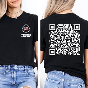 May include: Black t-shirt with a white American flag and the word "TRUMP" printed on the front. The back of the shirt has a white QR code printed on it.