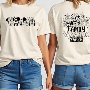 May include: Cream-colored t-shirt featuring a black and white graphic of Disney characters on the front and back. The front displays Minnie Mouse, Mickey Mouse, Goofy, and Pluto. The back says "Family Vacation 2026."