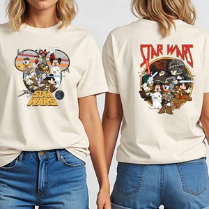 May include: Cream-colored t-shirt featuring a Star Wars graphic with Disney characters on the front and back. The front design includes Mickey Mouse, Donald Duck, and other characters in a circular design. The back features the Star Wars logo.