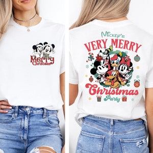 Puede incluir: Camiseta blanca con un dise&ntilde;o navide&ntilde;o con Mickey Mouse y Minnie Mouse en la parte delantera y Mickey Mouse, Minnie Mouse, Donald Duck, Goofy y Pluto en la parte trasera. El dise&ntilde;o de la parte trasera incluye el texto "Mickey's Very Merry Christmas Party".