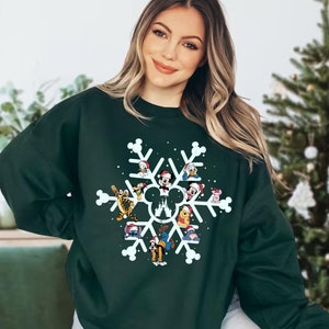 May include: A dark green sweatshirt with a white snowflake design featuring various Disney characters wearing Santa hats. The characters include Mickey Mouse, Minnie Mouse, Donald Duck, Goofy, Pluto, and others.