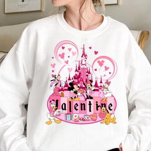 May include: White sweatshirt with a pink graphic of Mickey Mouse and friends in front of Sleeping Beauty's castle with the word "Valentine" printed below.