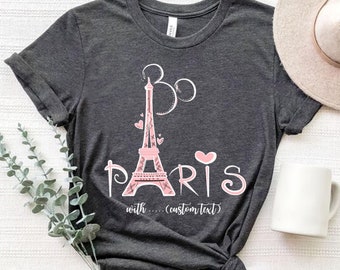 Könnte beinhalten: Ein dunkelgraues T-Shirt mit einem rosafarbenen Eiffelturm-Motiv und dem Text "Paris" mit einem rosafarbenen Herzen. Der Text "with... (custom text)" ist ebenfalls auf dem Shirt enthalten.