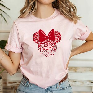 May include: A pink t-shirt with a red heart-shaped Minnie Mouse design. The design features a red bow and is made up of many small hearts.