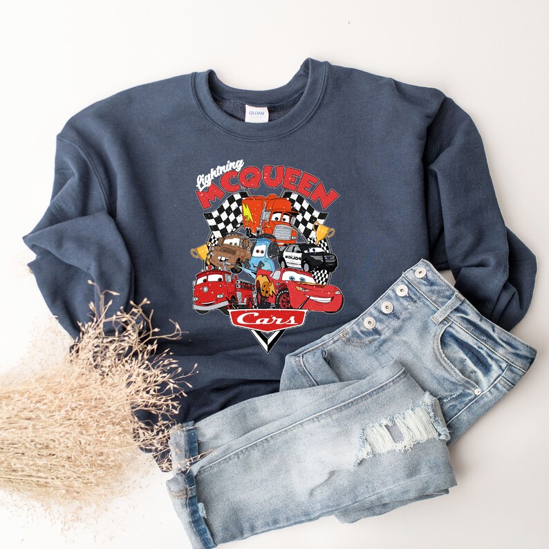 May include: A navy blue sweatshirt with a graphic of Lightning McQueen and other Cars characters. The graphic includes the text "Lightning McQueen" and "Cars".