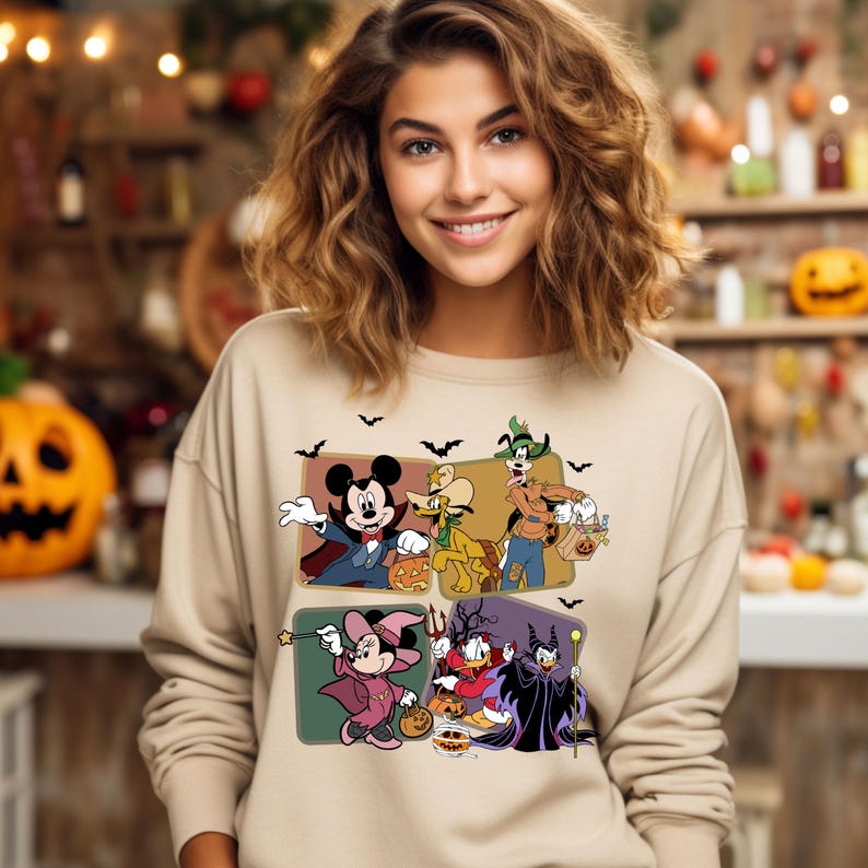 K&ouml;nnte beinhalten: Ein beiger Pullover mit einem Vintage-Druck von Mickey Mouse, Pluto, Goofy, Minnie Mouse und Donald Duck in Halloween-Kost&uuml;men. Die Figuren halten S&uuml;&szlig;igkeitent&uuml;ten und K&uuml;rbisse.