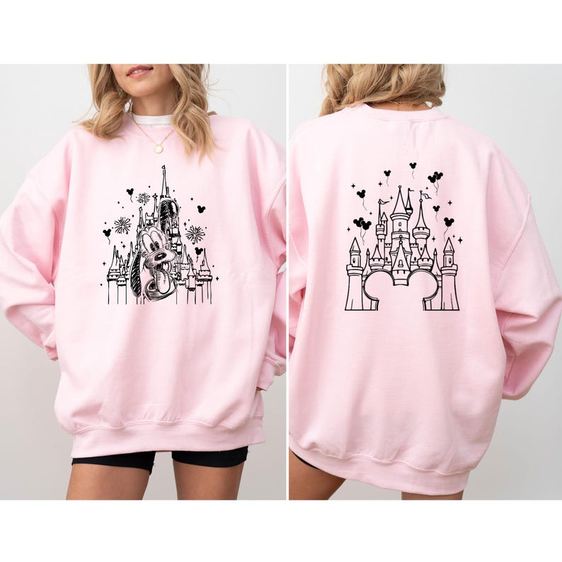 Puede incluir: Una sudadera rosa claro con un gr&aacute;fico negro de un castillo y un personaje de dibujos animados en la parte delantera y trasera. El gr&aacute;fico frontal incluye un personaje de dibujos animados y un castillo. El gr&aacute;fico trasero es un dise&ntilde;o de castillo.