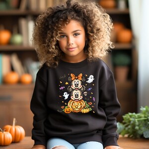 May include: Black Halloween sweatshirt with a stacked Minnie and Mickey Mouse design above a carved pumpkin. The design includes ghosts, sweets, and stars. The sweatshirt is worn by a young girl with curly hair.