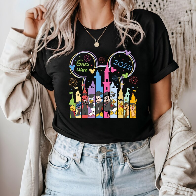 Puede incluir: Camiseta negra con un gr&aacute;fico colorido de orejas de Mickey Mouse, un castillo y personajes de Disney. El texto "Grad Liam 2025" est&aacute; dentro de las orejas de Mickey Mouse.